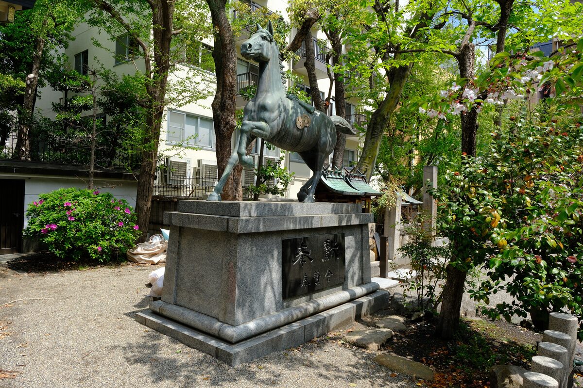 The bronze horse statue standing on its plinth among trees in the grounds of Namba Yasaka Shrine