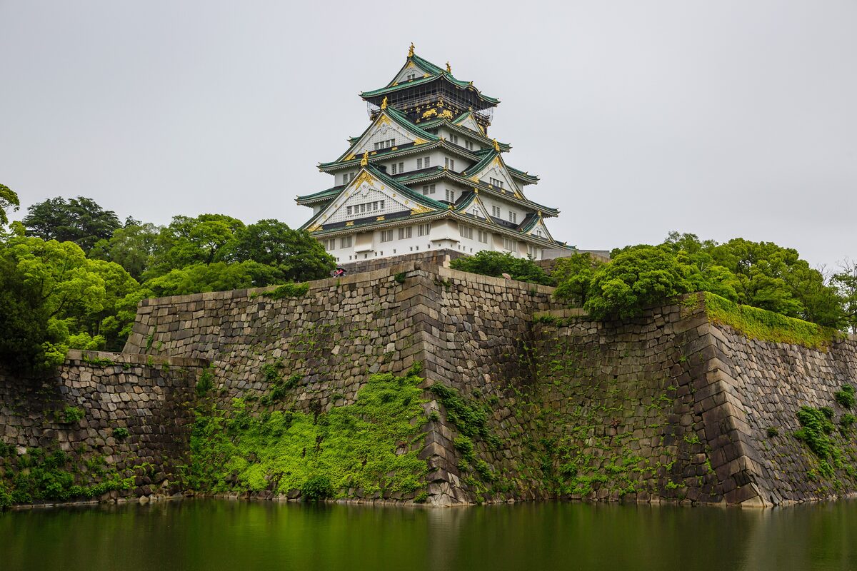 Osaka Castle's stone walls and white-and-green keep tower rising above the moat and trees