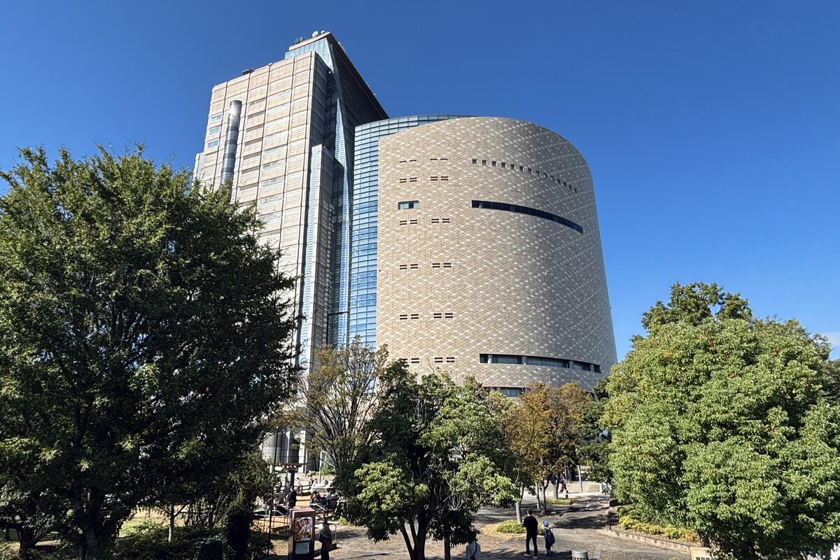 The round, tile-clad body of the Osaka Museum of History beside the glass NHK tower, framed by trees under a deep blue sky