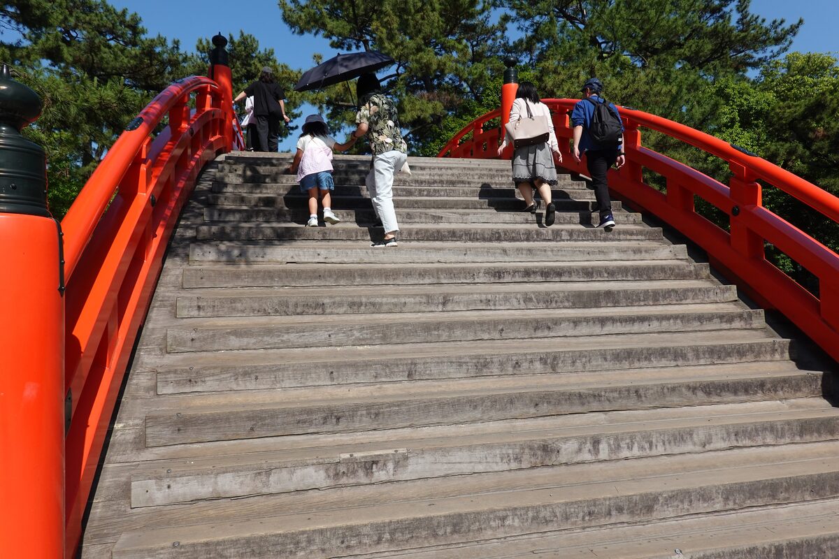 The steep stone steps of the red arched Sorihashi bridge at Sumiyoshi Taisha, with people climbing