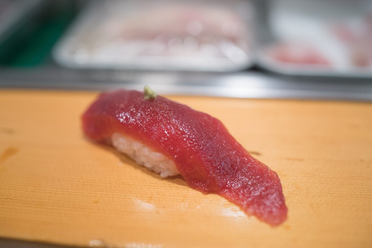 A piece of tuna nigiri sushi on a wooden board