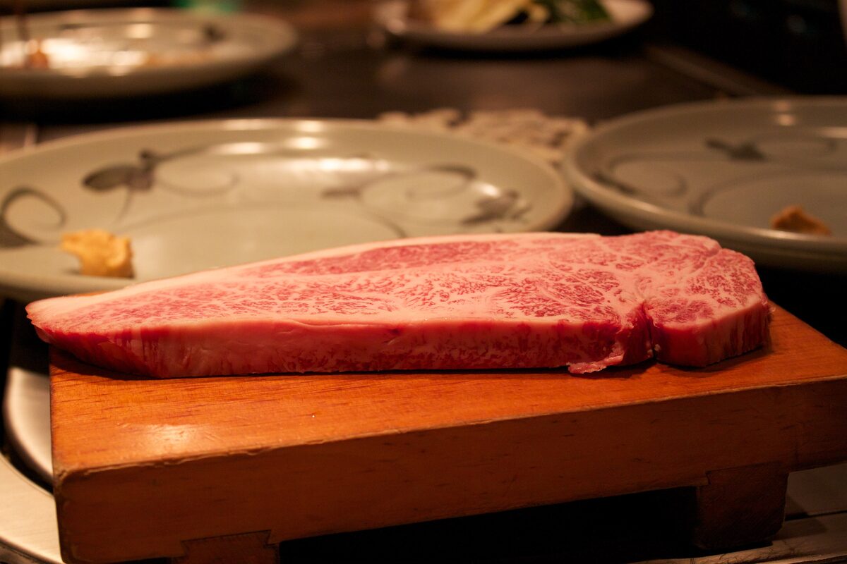 A raw, heavily marbled slab of wagyu beef on a wooden board, ready for the grill