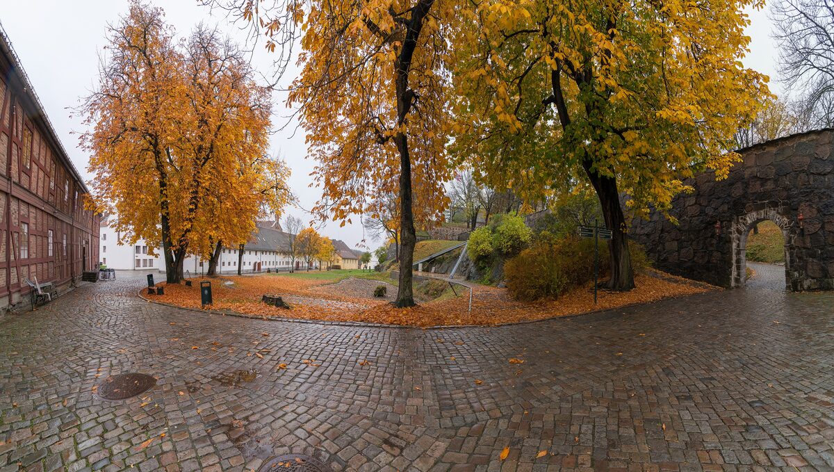 A cobbled courtyard inside Akershus Fortress with autumn trees and an old stone archway