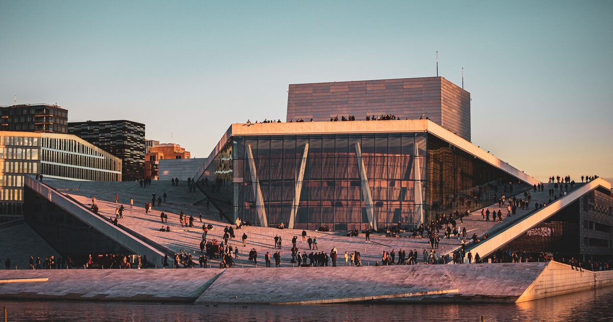 The white marble roof of the Oslo Opera House sloping down to the water at sunset, with people walking on it