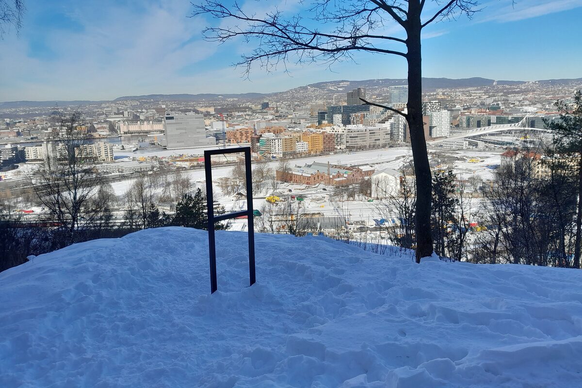 An empty steel frame on a snowy hilltop in Ekebergparken, looking over the rooftops of Oslo