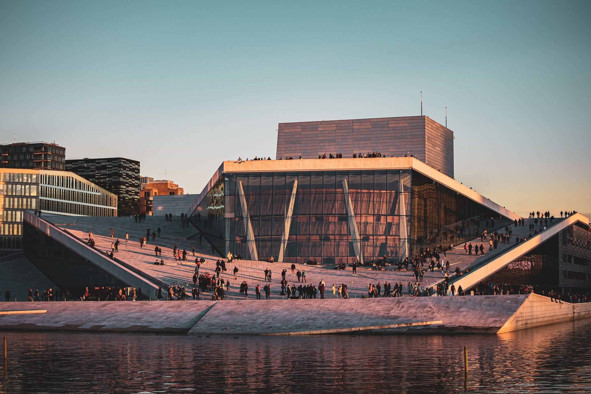 The white marble roof of the Oslo Opera House sloping down to the water at sunset, with people walking on it
