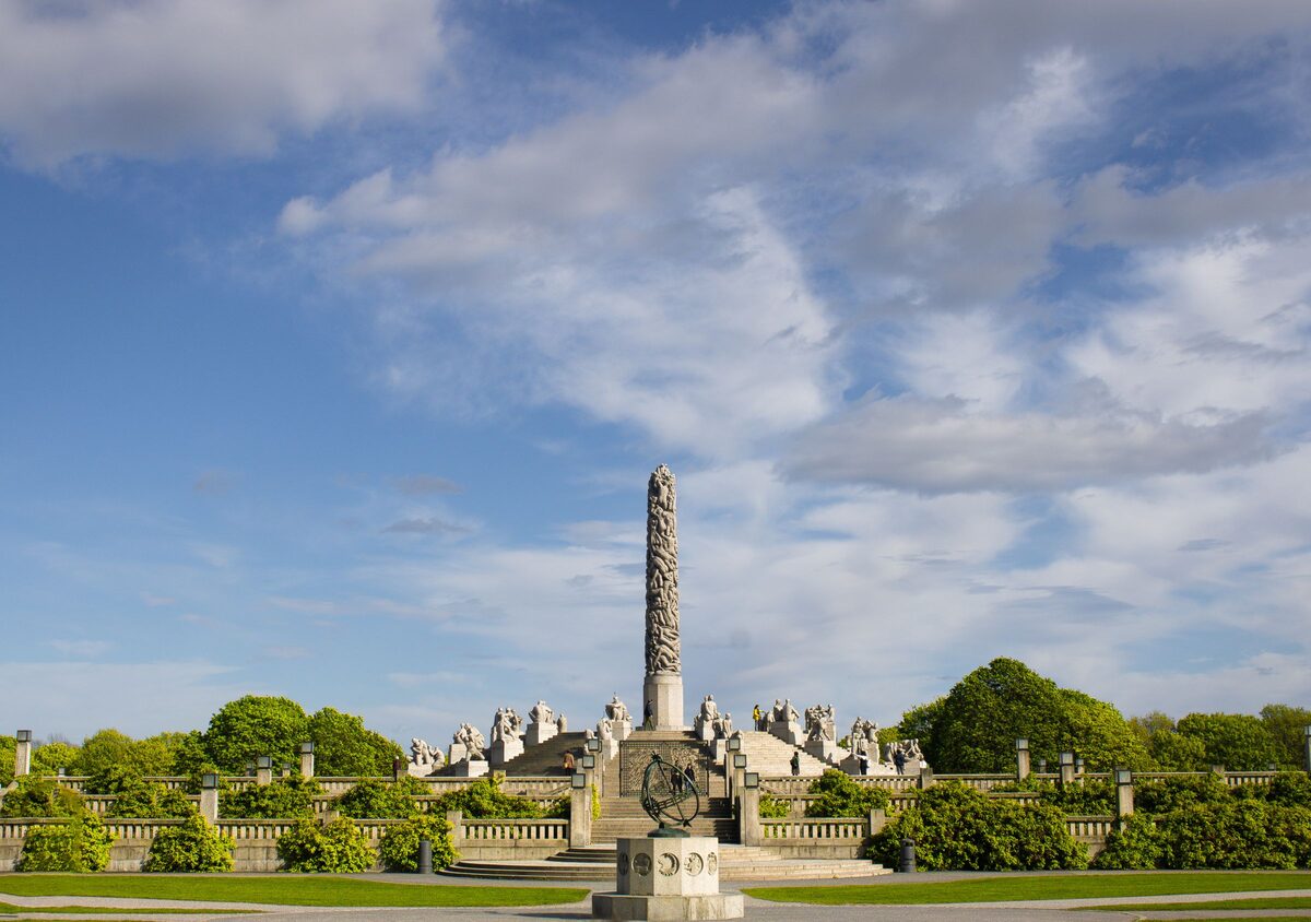The granite Monolith of Vigeland Park rising above stone sculptures and green hedges under a blue sky