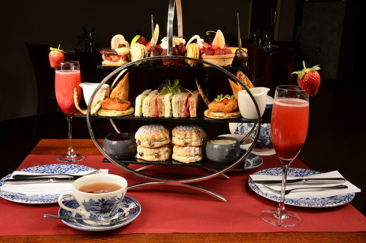 A tiered stand of sandwiches, scones and small cakes with teacups on a red tablecloth