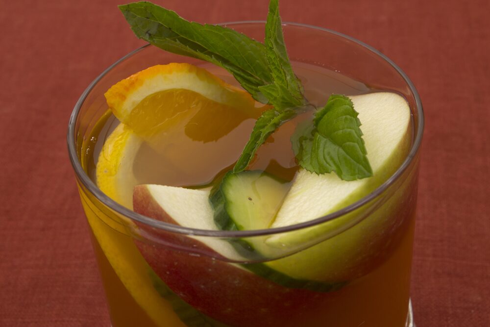 A glass of Pimm's with slices of orange, apple and cucumber and a sprig of mint