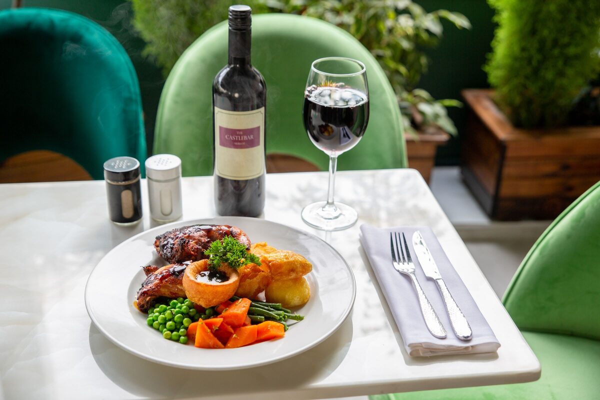 A plate of roast beef with a Yorkshire pudding, roast potatoes, peas and carrots, with a glass of red wine