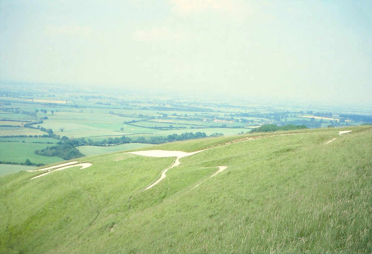 The stylized white chalk horse cut into the green hillside at Uffington, with farmland stretching away below