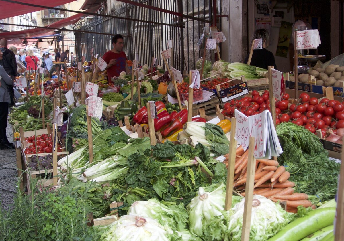 Vegetable stalls along a Capo market lane, with chard, peppers, tomatoes and carrots