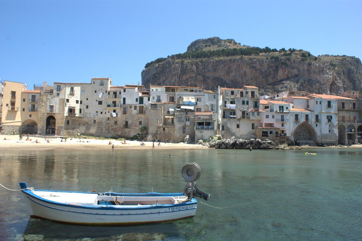 Cefalù's small sandy beach and a wooden boat, with La Rocca behind