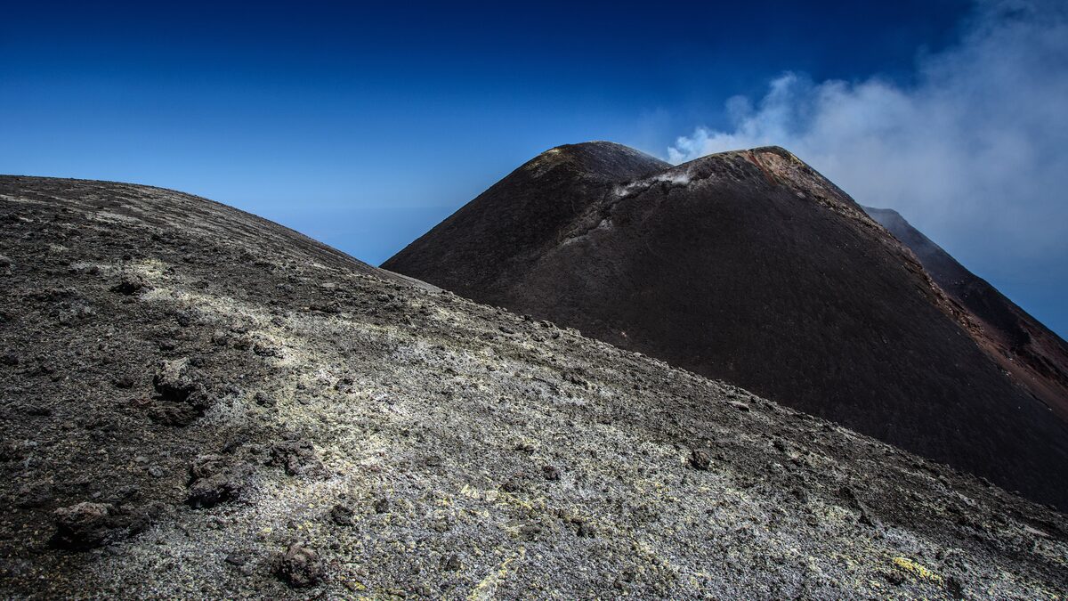 The black summit crater of Mount Etna with a plume of steam