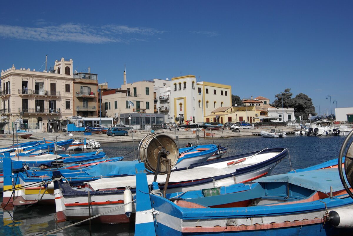 Blue-and-white fishing boats in Mondello's small harbor, with houses behind