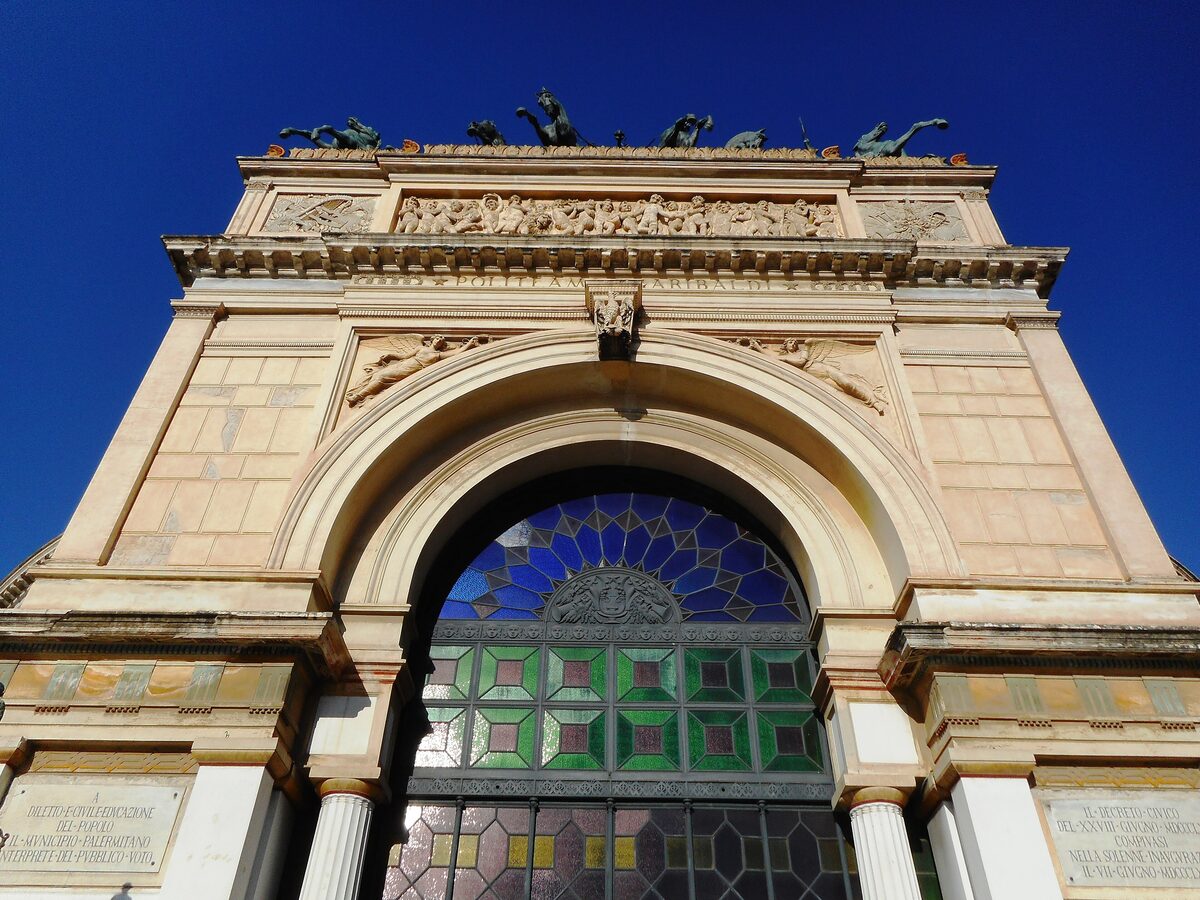 The triumphal arch of the Teatro Politeama against a deep blue sky