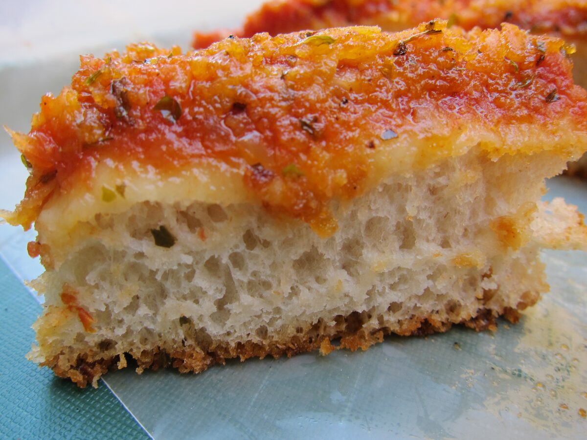 A thick slice of sfincione with a tomato and onion topping and a spongy base