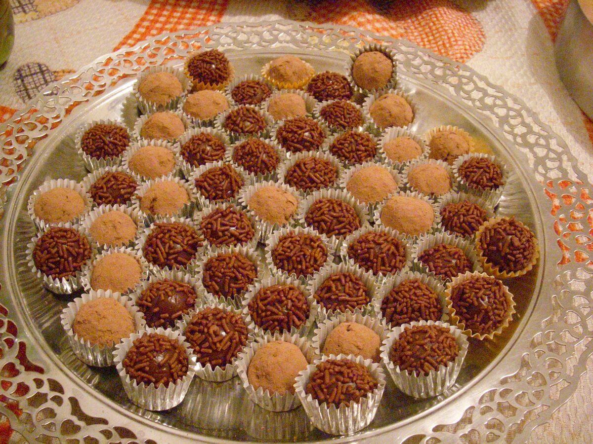A silver platter of brigadeiros in paper cases, most rolled in chocolate sprinkles