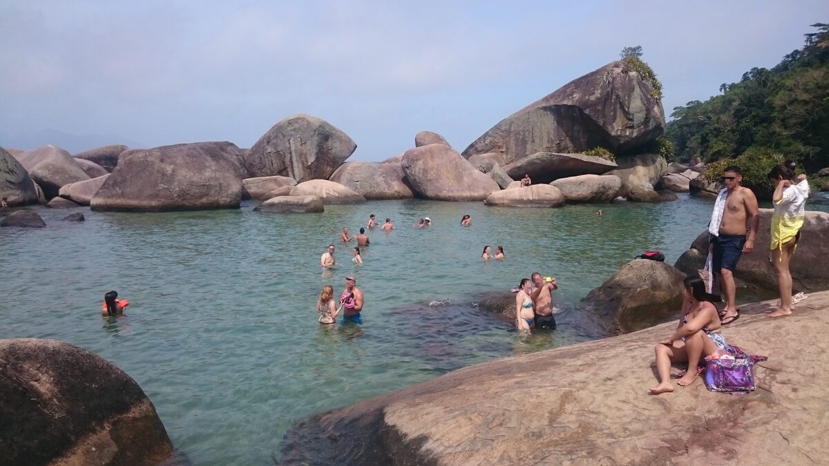 Swimmers in the natural rock pool of Cachadaço, a clear basin between granite boulders