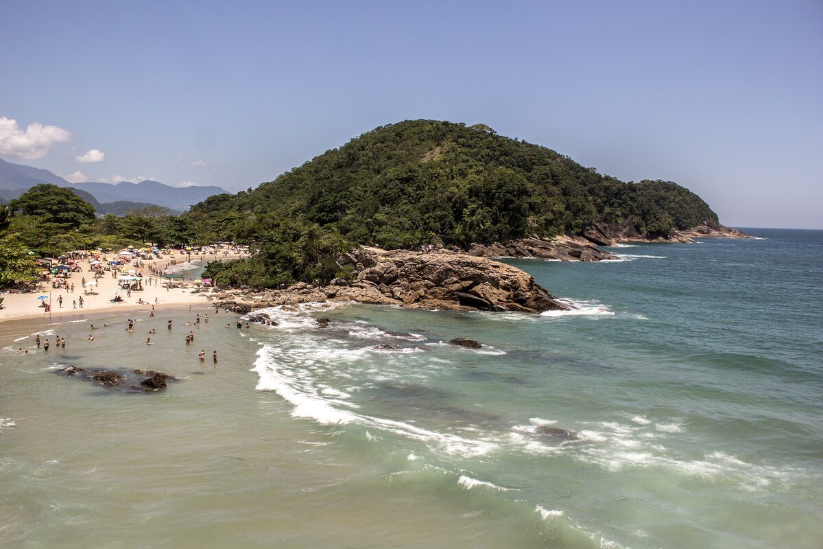 Praia do Meio in Trindade, a sandy cove with a wooded headland and surf breaking on the rocks