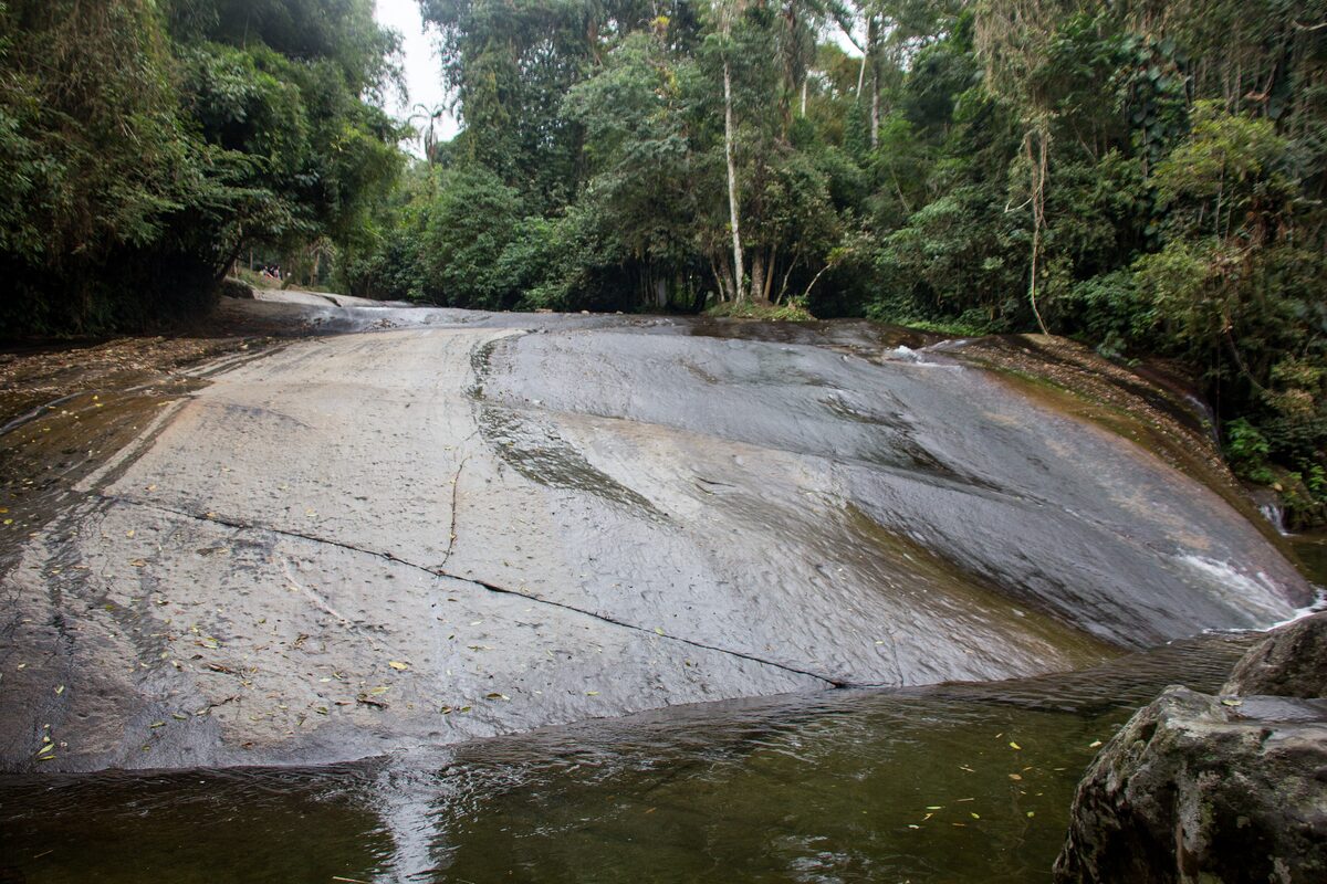 A wide, smooth granite slab sloping into a forest pool, the natural water slide near Paraty