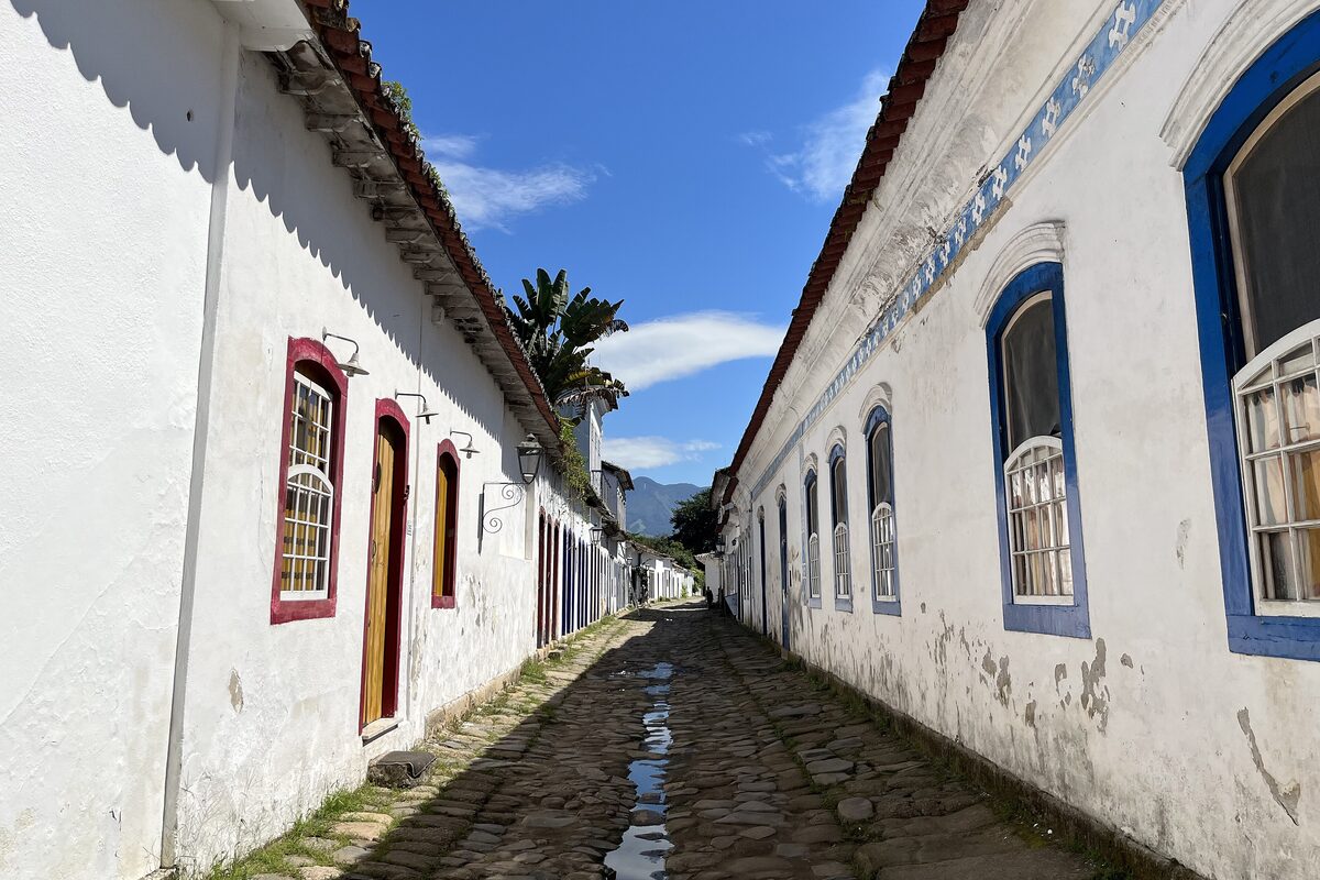 A cobbled street in the Paraty historic center, lined with white colonial houses and blue window frames