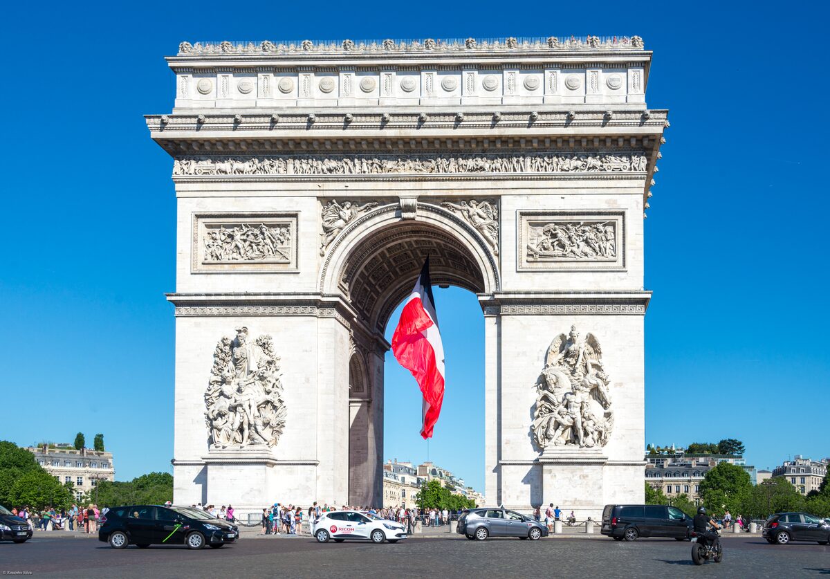 The Arc de Triomphe with the French flag under its central arch and traffic around it