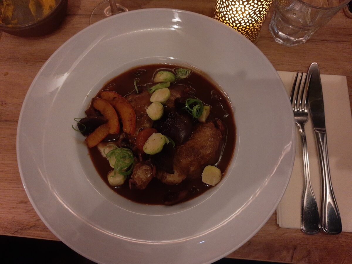 Chicken braised in dark red-wine sauce with carrots and small onions, on a white plate