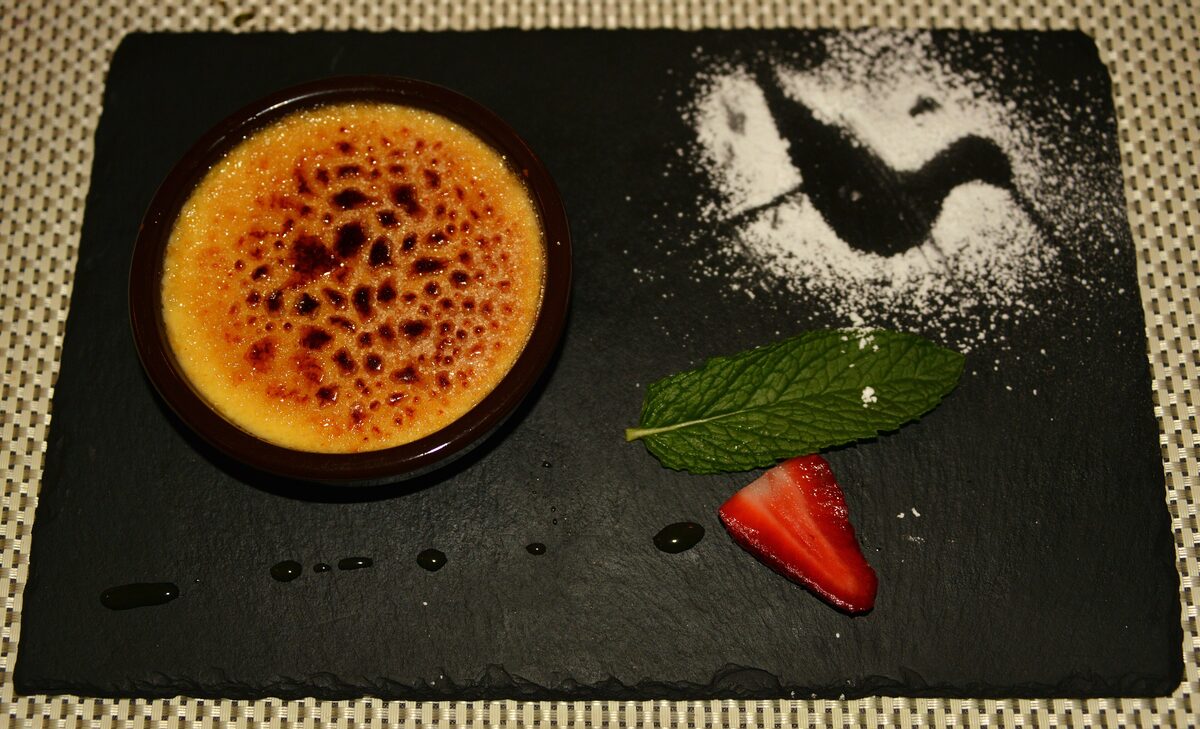 A crème brûlée with a caramelized sugar top, served with a mint leaf and a strawberry on slate