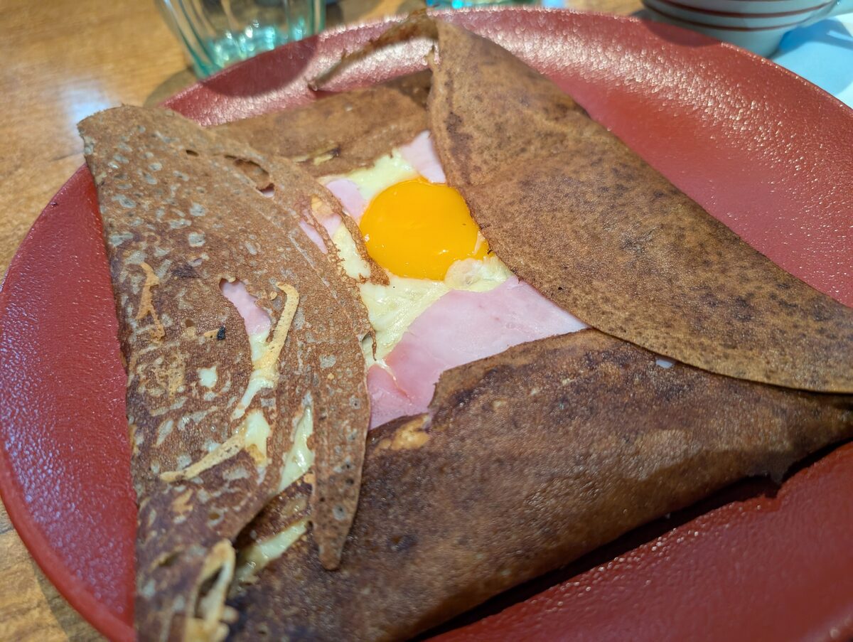 A buckwheat galette folded around ham, cheese and a fried egg on a red plate, as served in Brittany