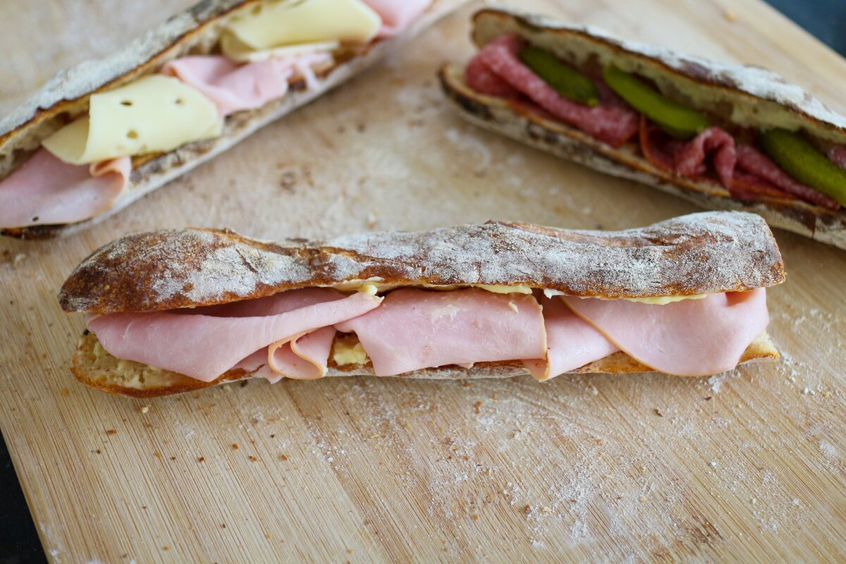 A baguette sandwich filled with sliced ham and butter on a wooden board