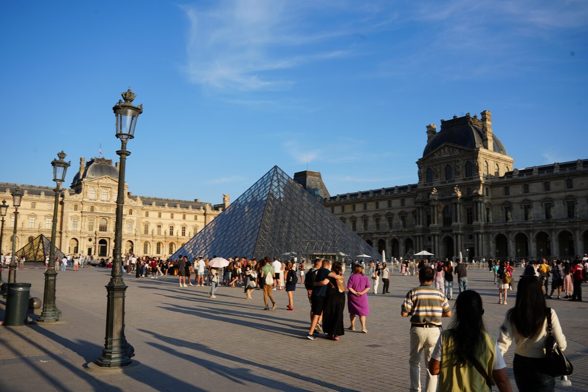 The glass pyramid and the Denon wing of the Louvre, with visitors crossing the courtyard