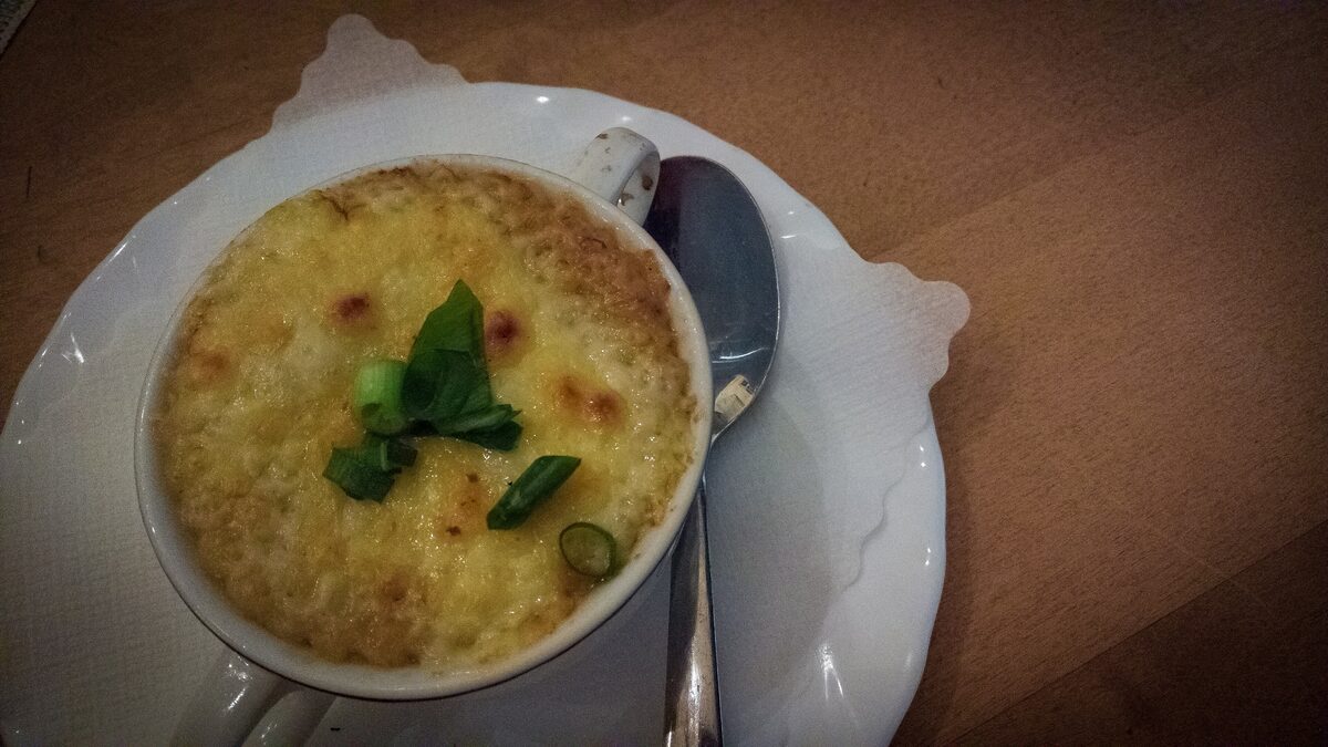 Onion soup in a bowl under a golden crust of melted cheese, with a sprig of herb on top