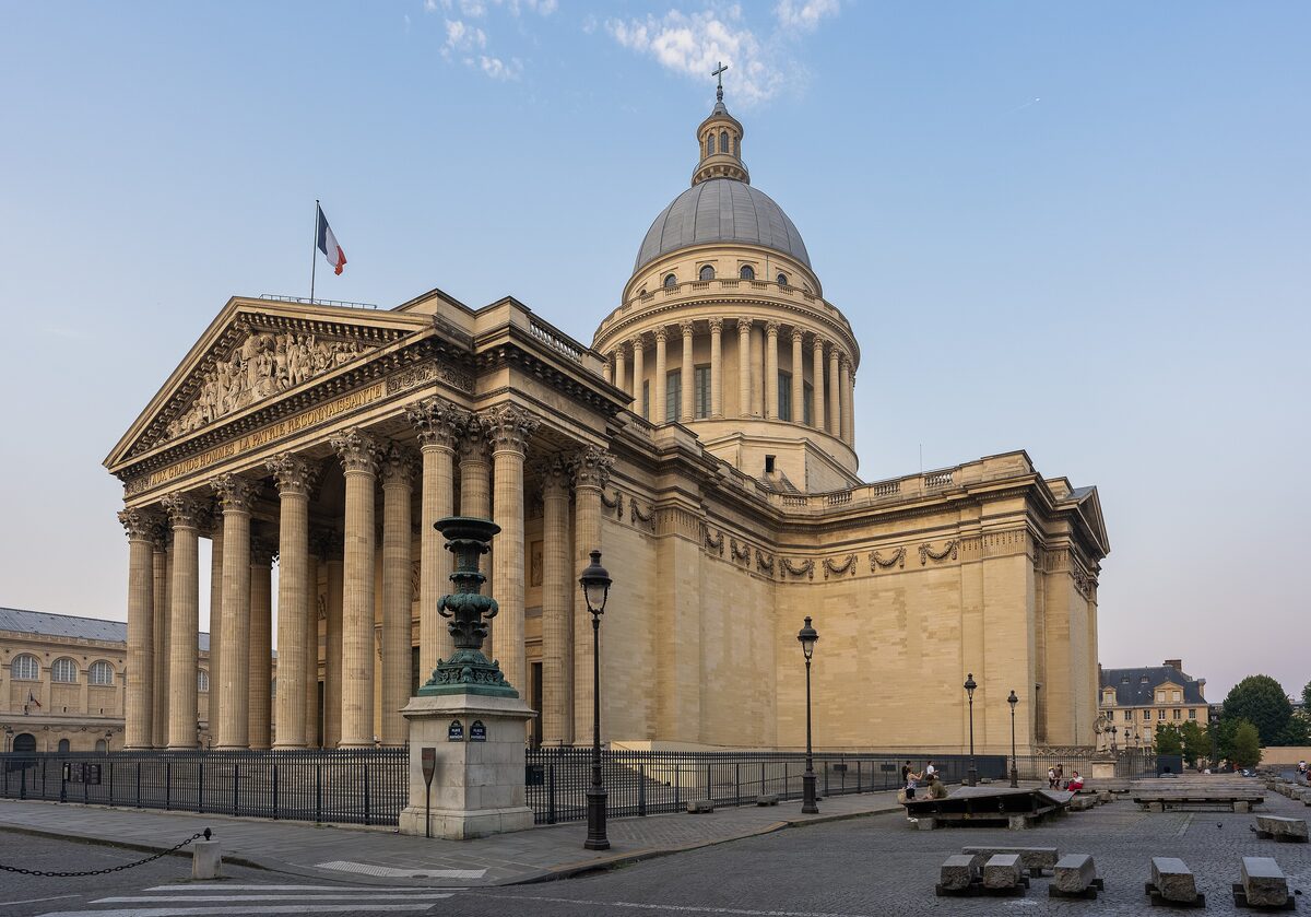 The Panthéon's columned portico and grey dome in daylight, with a flag flying and an empty square in front