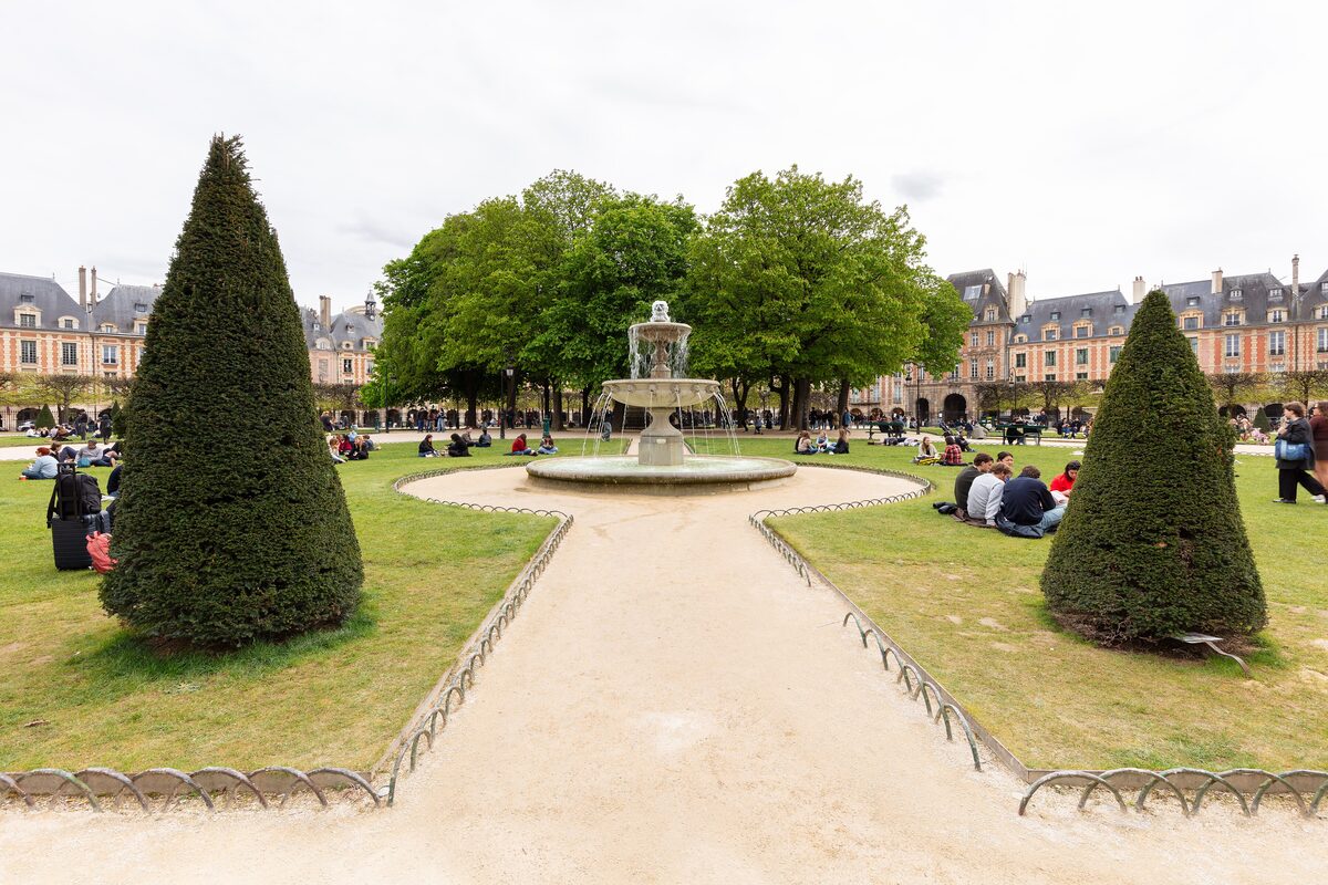 The fountain and clipped cones on the lawn of Place des Vosges, with the arcaded houses behind