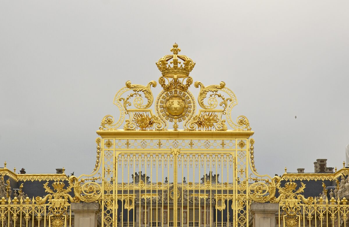 The gilded wrought-iron Golden Gate of the Palace of Versailles, with the palace roofs behind