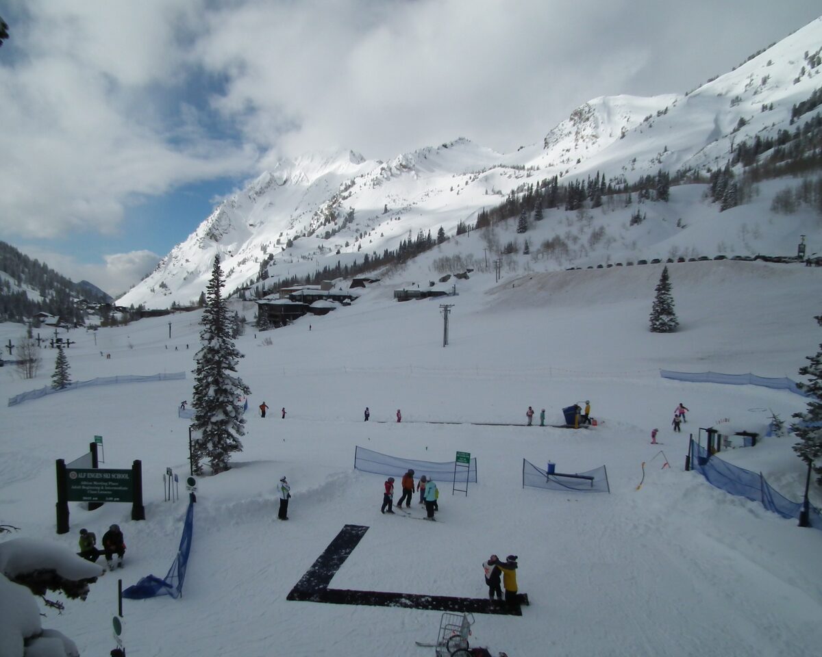 Skiers at the snowy base area of Alta, with steep peaks rising behind