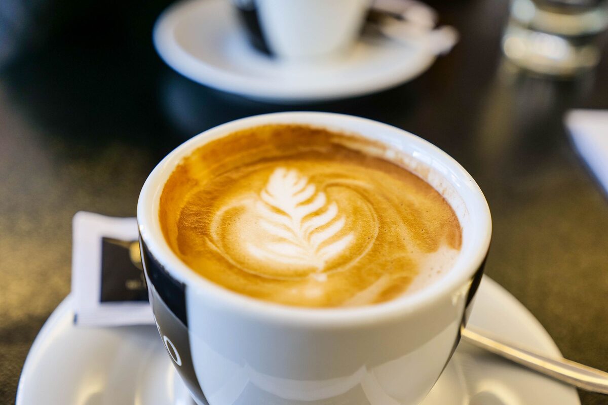 A cup of latte with leaf-shaped foam art on a saucer