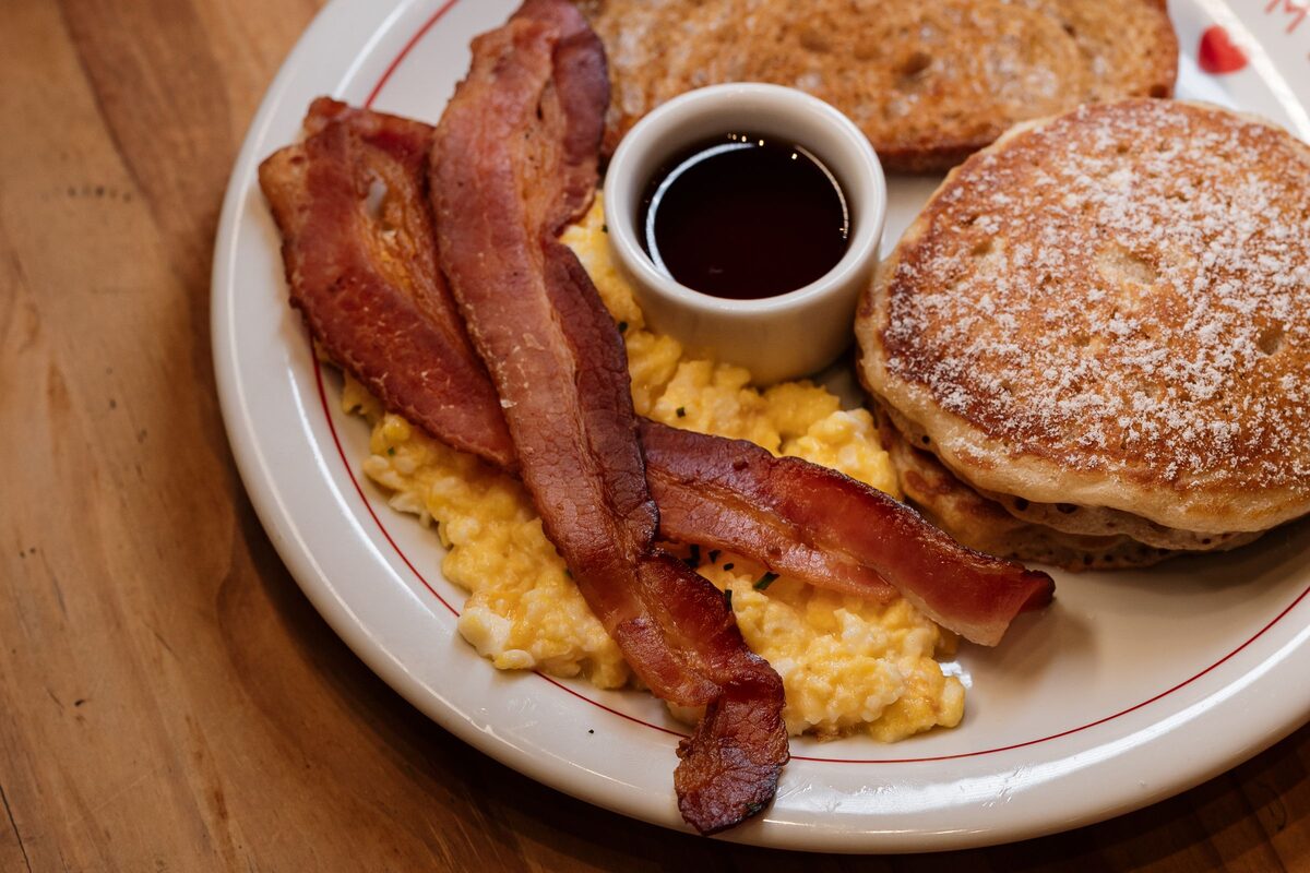 A diner breakfast plate of pancakes, scrambled eggs, bacon and maple syrup