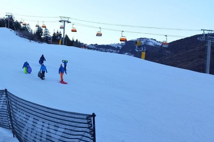 Orange-hooded chairs running over a snowy slope at Canyons Resort at dusk, with people carrying sleds up the hill
