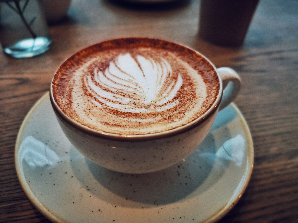 A cappuccino with a leaf pattern in the foam on a stone-glazed saucer on a wooden table