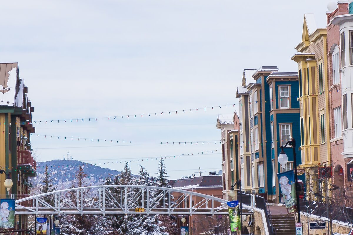 A footbridge and the colorful buildings of Main Street in Park City, with snow on the hills behind