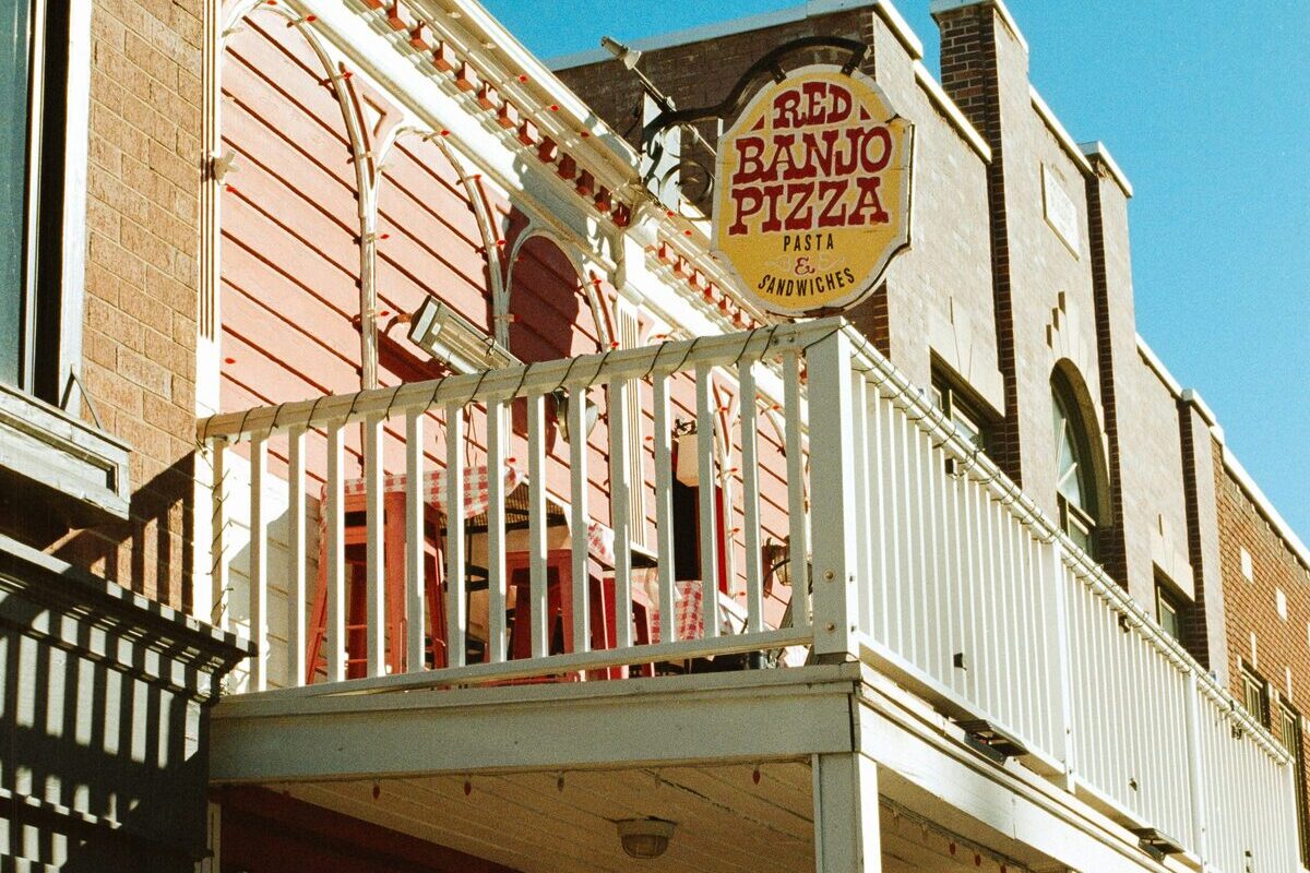 The balcony and round Red Banjo Pizza sign on the front of the restaurant on Main Street