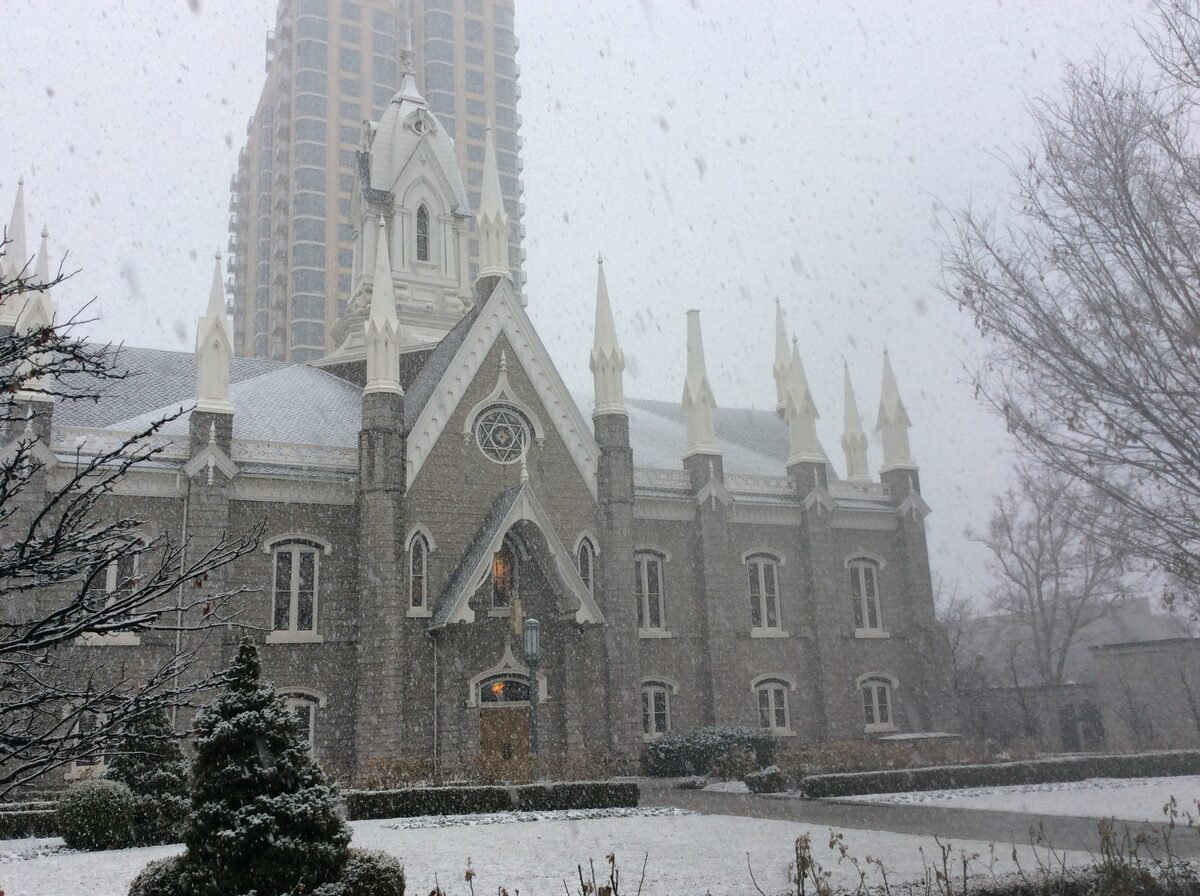 The Salt Lake Assembly Hall on Temple Square in falling snow, with a tower block behind
