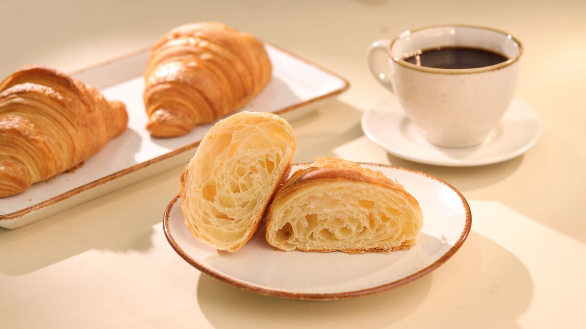 Golden croissants, one torn open to show the layers, beside a cup of black coffee
