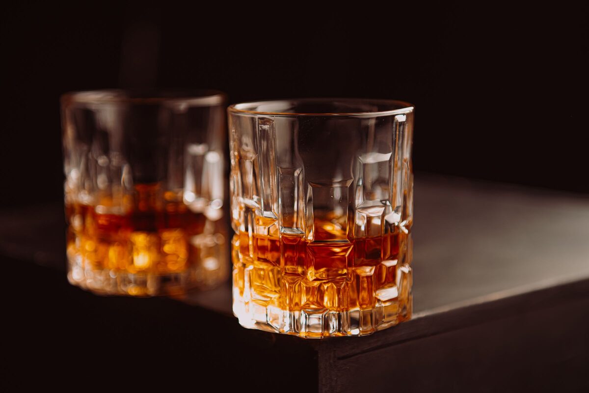 Two cut-glass tumblers of amber whiskey on a dark bar top