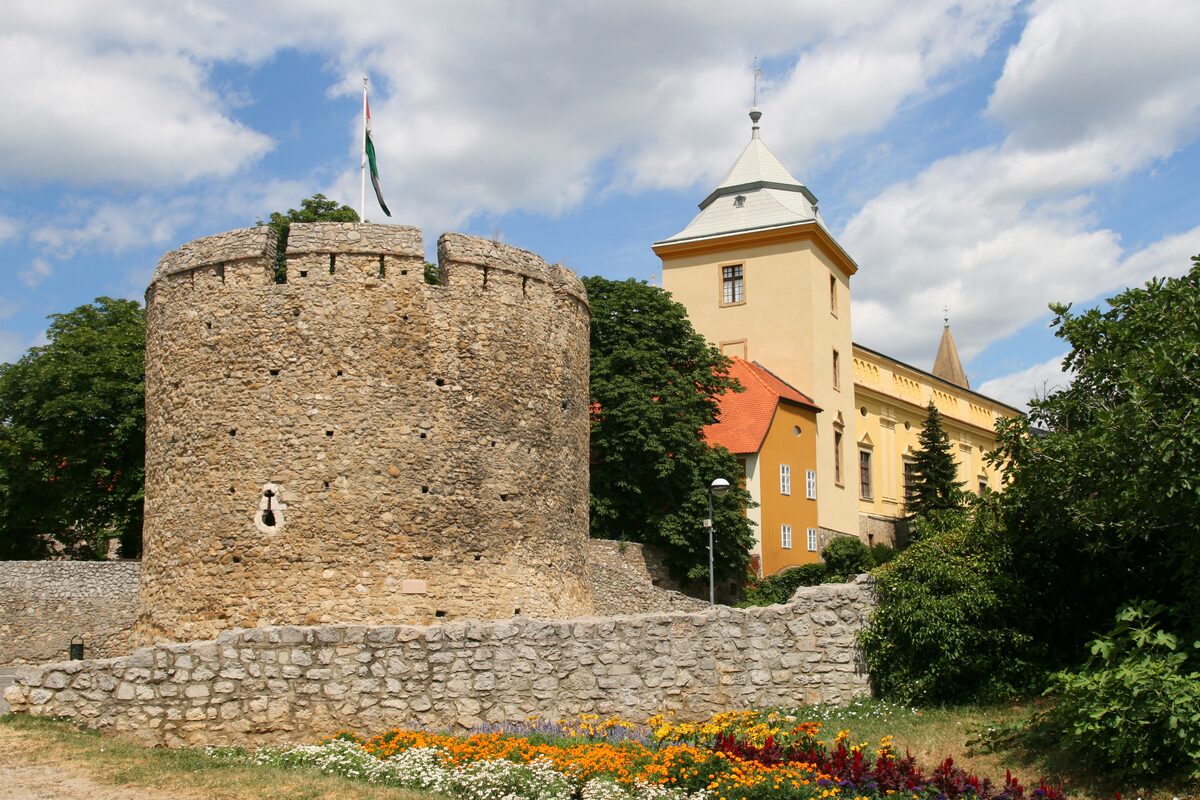 The round stone Barbakán bastion in Pécs with flower beds in front and a yellow tower behind