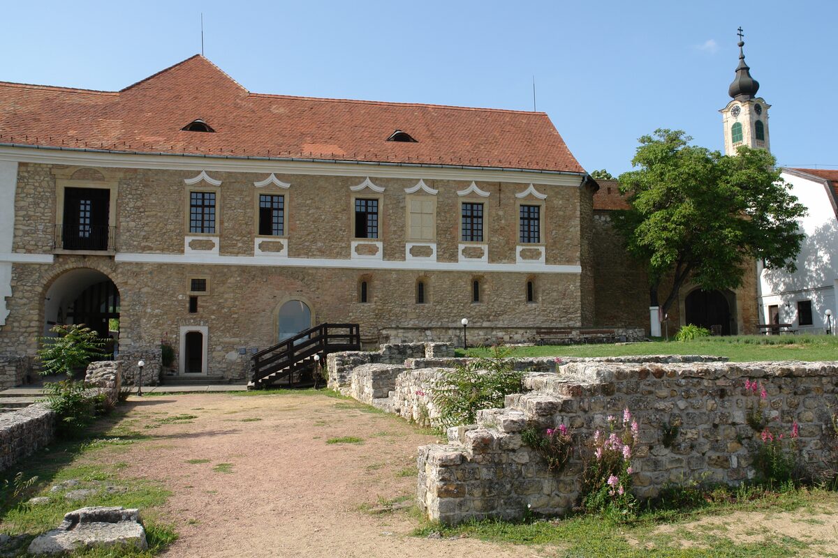 The stone castle of Pécsvárad with a red roof and the excavated walls of the abbey in front