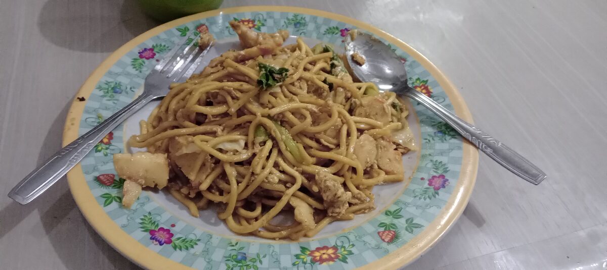 Yellow noodles fried in dark soy on a floral plate, a vegetarian version of Hokkien mee