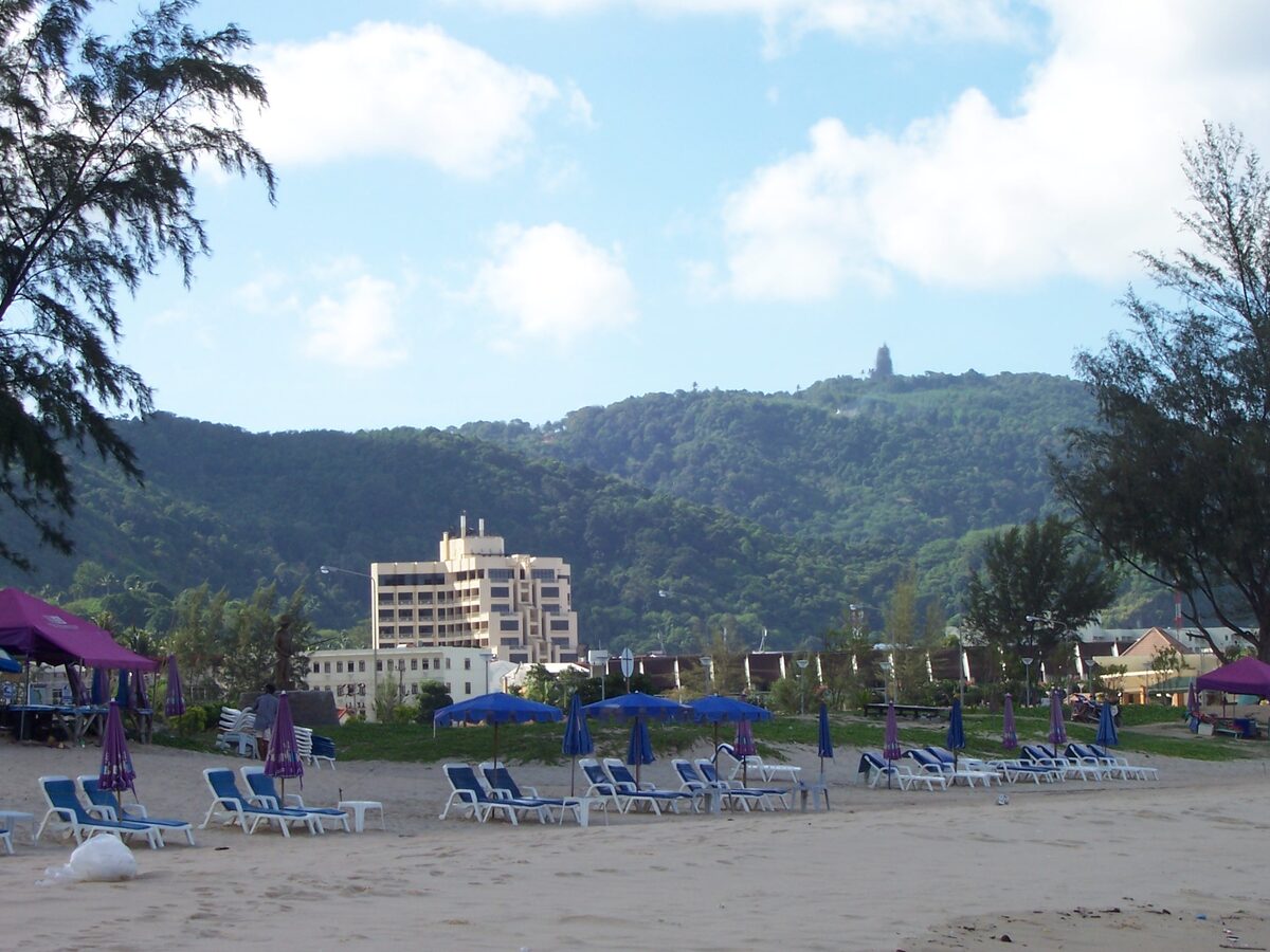 Sun loungers and a hotel on the sand at Karon Beach, with a green hill behind
